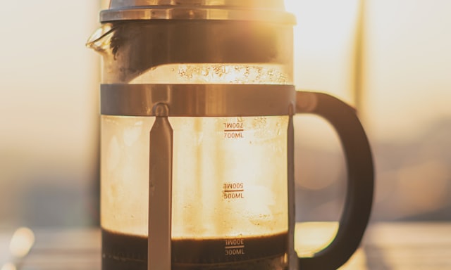 A French press of brewed coffee backlit by sunlight