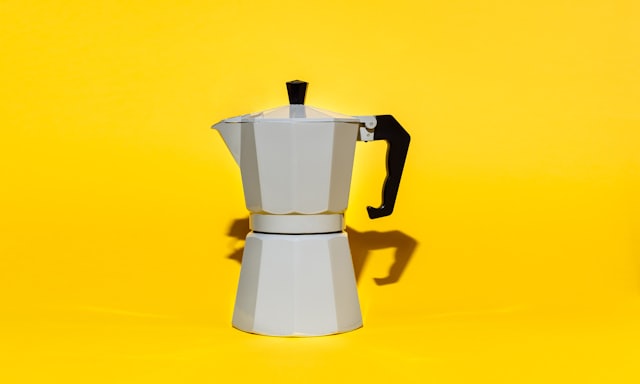 A moka pot against a bright yellow background
